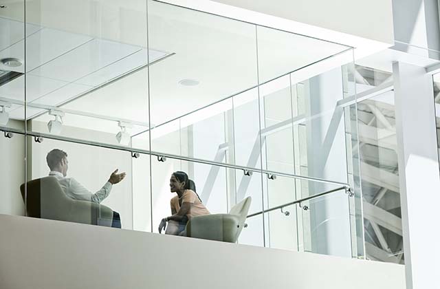 Businessman and woman standing behind a conference room window ina large business center